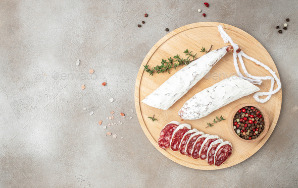 Fuet, traditional spanish dry cured sausage on a wooden board on a light background