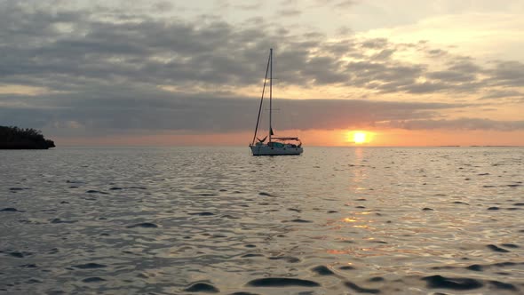 Cinematic Aerial View, Sailboat Anchored in Sea by Island Coast With Picturesque Sunset on Horizon, alt