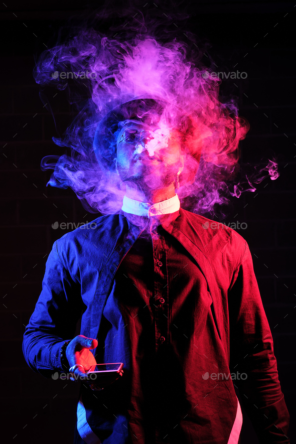 Ethnic man exhaling smoke on dark background