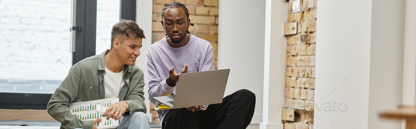 african american man showing project on laptop to male colleague, sitting on stairs, startup, banner