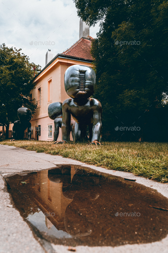 Crawling babies in Prague\'s Kampa park, with old sculptures reflecting in a puddle.