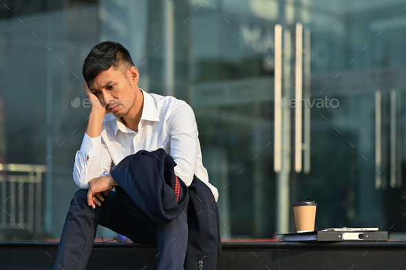 Upset man sitting on stairs outside office building, lost job due financial crisis employee.