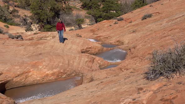 Hiking on sandstone viewing woman hiking up past frozen pools of water alt