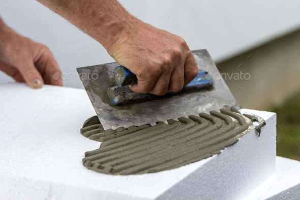 Close-up of worker hand with trowel applying glue on white rigid polyurethane foam sheet