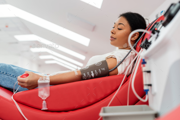side view of multiracial woman in pressure cuff and transfusion set holding rubber ball