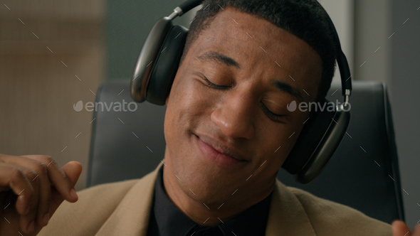 Carefree relaxed African American man happy businessman in headphones listen song dancing to music