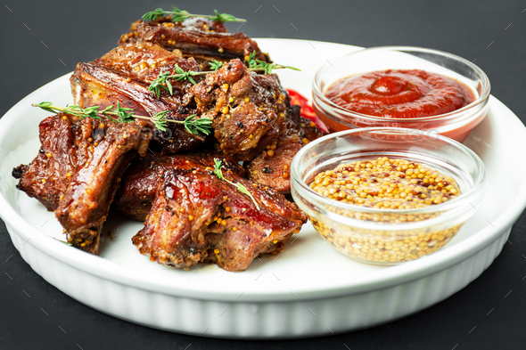 Baked ribs on a white plate. Roasted pork ribs with spices on a dark background. Food background