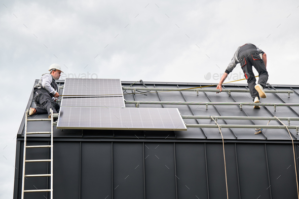 Man worker mounting solar panels on roof of house.