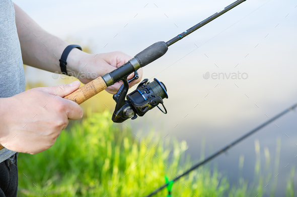 A fishing rod with a spinning reel in the hands of a fisherman. Fishing.  Outdoor recreation. Stock Photo by Art-Family