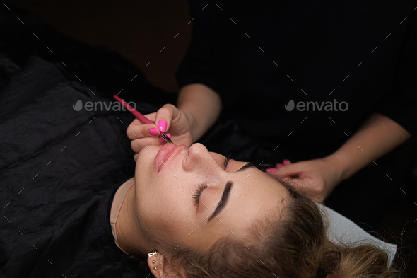 The master with a brush applies a toning paste to the lip contour Delicate permanent lip makeup
