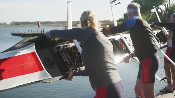 Rowing team of four senior caucasian men and women lowering boat into river alt