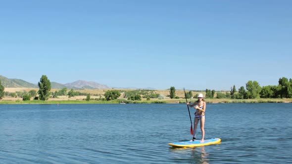 Young woman learning how to paddleboard on small pond. alt