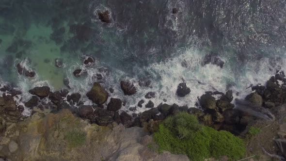 Top view on a Peguyangan waterfall against a background of crashing waves on a rocky shore. alt