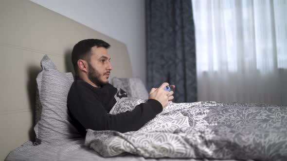 Quarantined Young Man Playing Video Games in Bed Using Controller alt