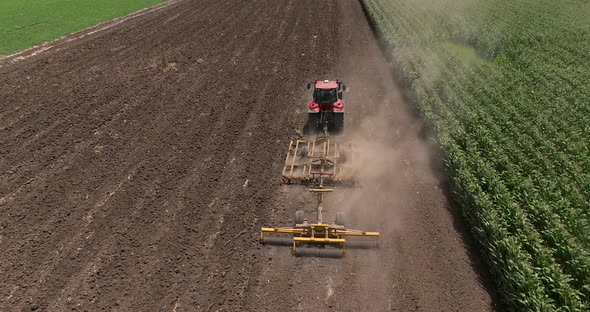 Red tractor flattening a field for seeding, Drone follow footage. alt