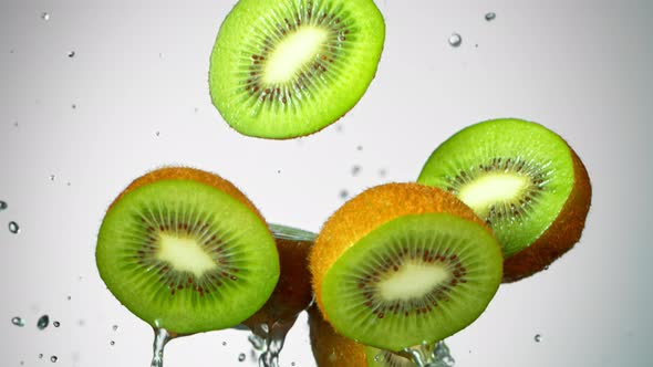 Super Slow Motion Shot of Flying Kiwi Slices and Splashing Water on Grey Background at 1000Fps alt