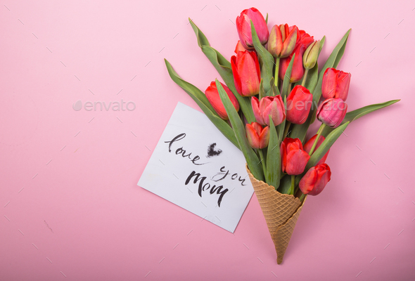 red beautiful tulips in an ice cream waffle cone with card Love you mom on a color background.