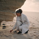 Woman writing beach sand at shore cliff rock. Black hair tourist resting ocean - PhotoDune Item for Sale