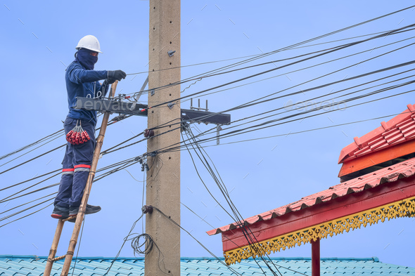 Asian technician on ladder installing cable lines to connect internet signal system on electric pole