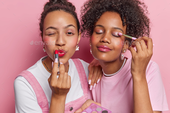 Photo of female friends apply red lipstick and eyeshadow put on makeup use cosmetic brush stand next