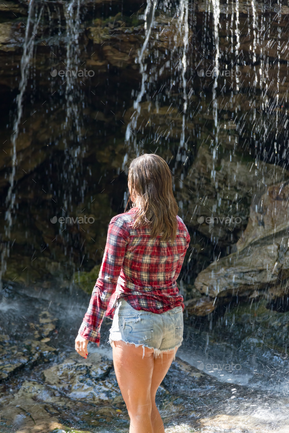 Beautiful young woman in cut-off jeans and red flannel shirt walking across rocks