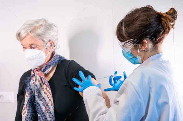 Elderly woman receiving the injection of the coronavirus vaccine by a doctor