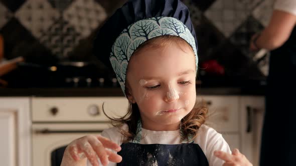 Cute Little Girl Smeared with Flour Licks Her Fingers with Dough in the Kitchen. alt