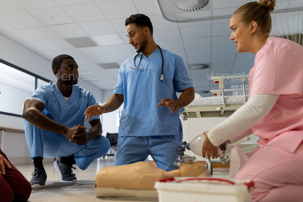 Biracial male doctor with diverse trainee doctors learning cpr on model at hospital