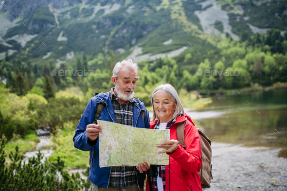 Senior tourists with backpacks reading map, preparing for hike.