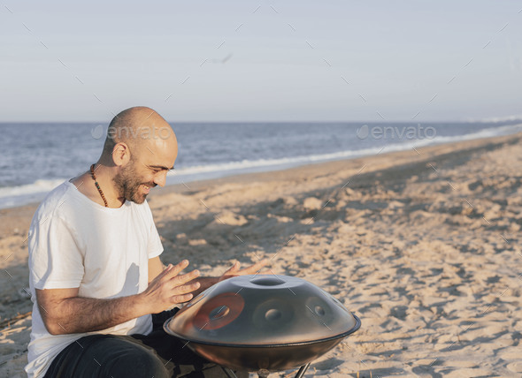 happy man playing handpan on the beach, sea behind him, concept of meditation and relaxation.