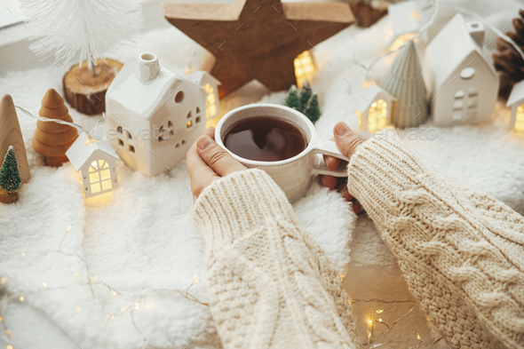 Cozy winter. Hands in sweater holding stylish cup of tea with