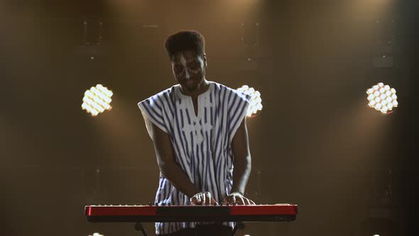 African American Man Plays Piano Synthesizer Keyboard and Sings in Dark Studio with Bright Lights alt