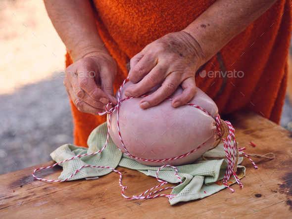 Crop elderly woman tying sobrassada with thread in farmyard