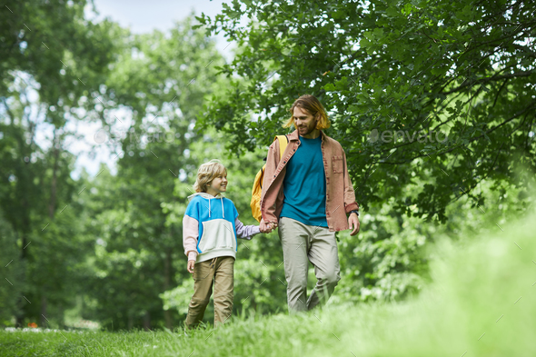 Happy Father And Son Holding Hands Walking On Green Grass In Park