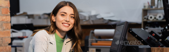 cheerful woman smiling near monitor while working in print center, banner