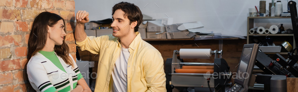 cheerful man flirting with pretty colleague while standing together in print center, banner