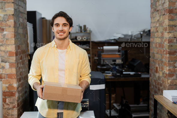 happy man holding carton box and looking at camera in print center