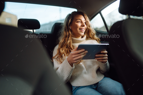 Young woman sitting in back seat of car with tablet in hand. Business, technologie, online concert.