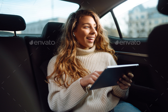 Young woman sitting in back seat of car with tablet in hand. Business, technologie, online concert.