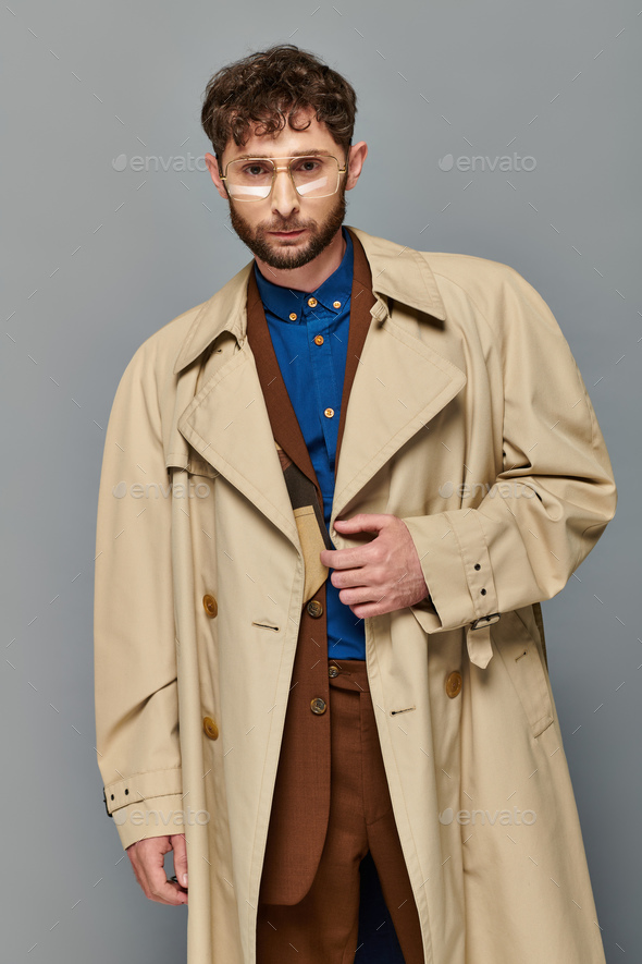 full length view of fashionable man in trench coat holding hands in pockets  while posing on grey | Stock image | Colourbox