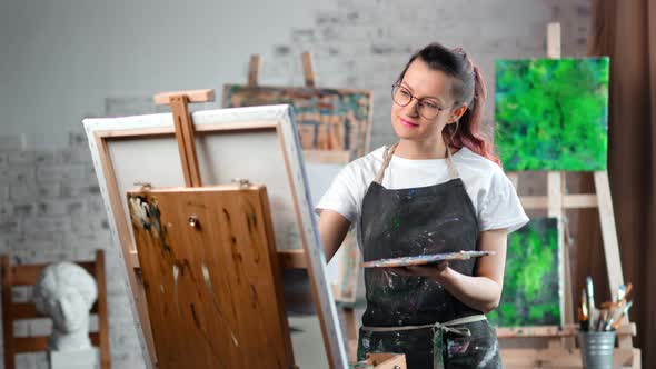 Happy Hipster Creative Female Painter Enjoying Drawing Picture on Canvas at Art Studio Medium Shot alt