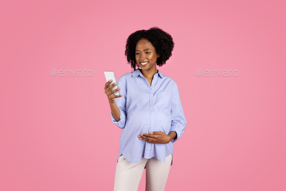 Cheerful young black pregnant woman in casual touch belly, use smartphone, chatting in social