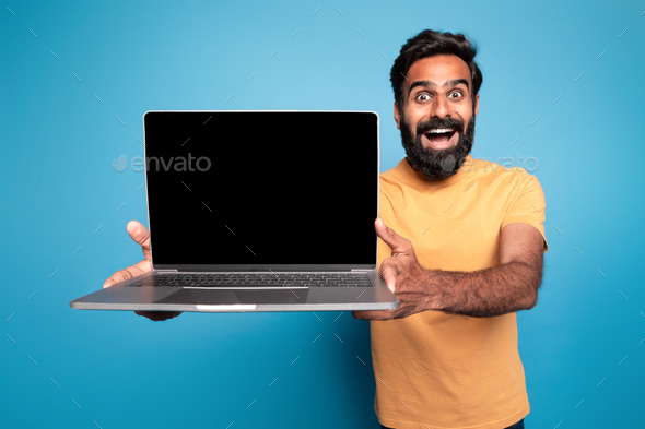 Great website. Excited middle aged indian man holding laptop computer with blank screen and