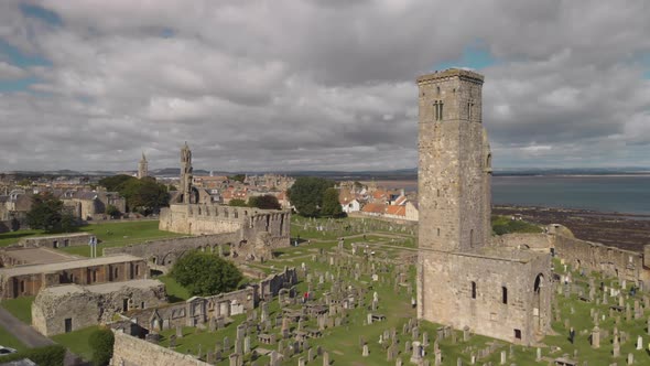 Aerial drone flying by one of the towers of the St Andrews Cathedral as other towers and the coastli alt