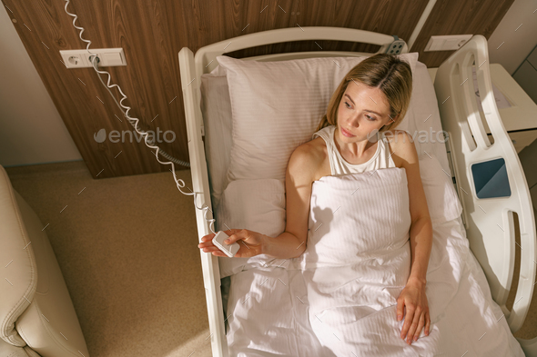 Top view of woman patient holding emergency call button while lying in hospital bed