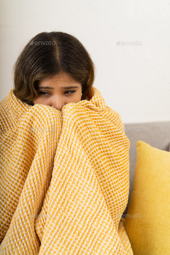 Woman hidden behind a blanket with an expression of anxiety Stock Photo