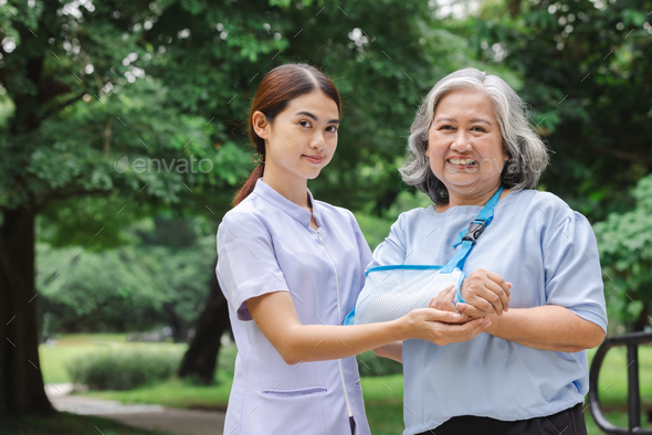 Senior Asian woman wearing patient gown and soft splint due to sore arm, personal accident concept.