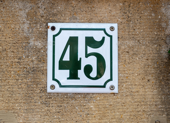 White metal sign with black number digit 45 bolted on rough brown plastered cement wall background.