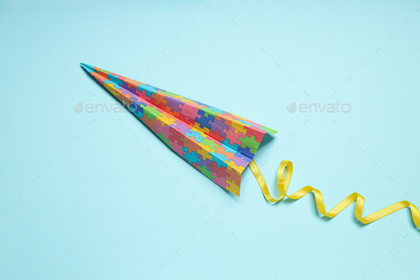 Paper plane with colorful puzzle pieces on light background. World autism day concept