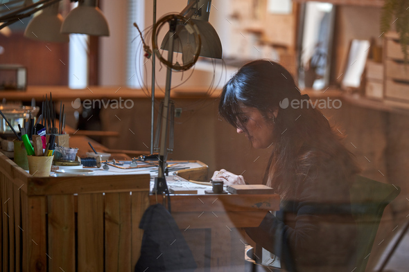 Attentive ethnic female goldsmith working with various tools in